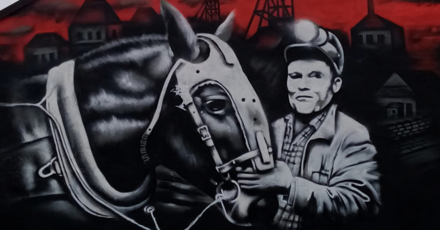 Black and white mural depicting a miner holding a horse's bridle, with a red background.
